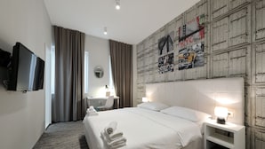 Habitación de hotel con una cama grande, una mesita de noche con lámpara, un televisor de pantalla plana montado en la pared, un escritorio con silla y una ventana con cortinas.