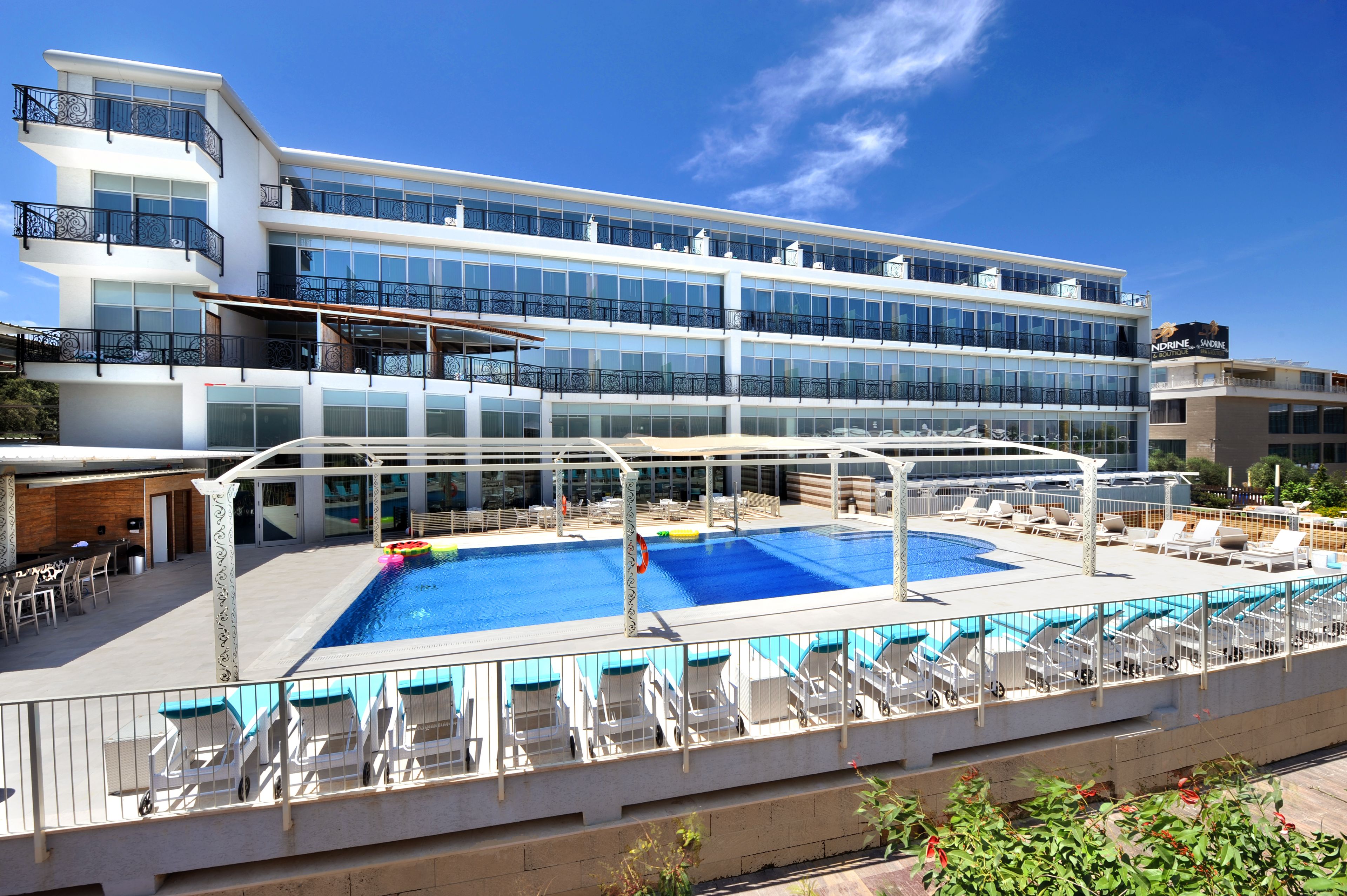 Um hotel moderno com piscina no terraço, várias varandas e um céu azul límpido.