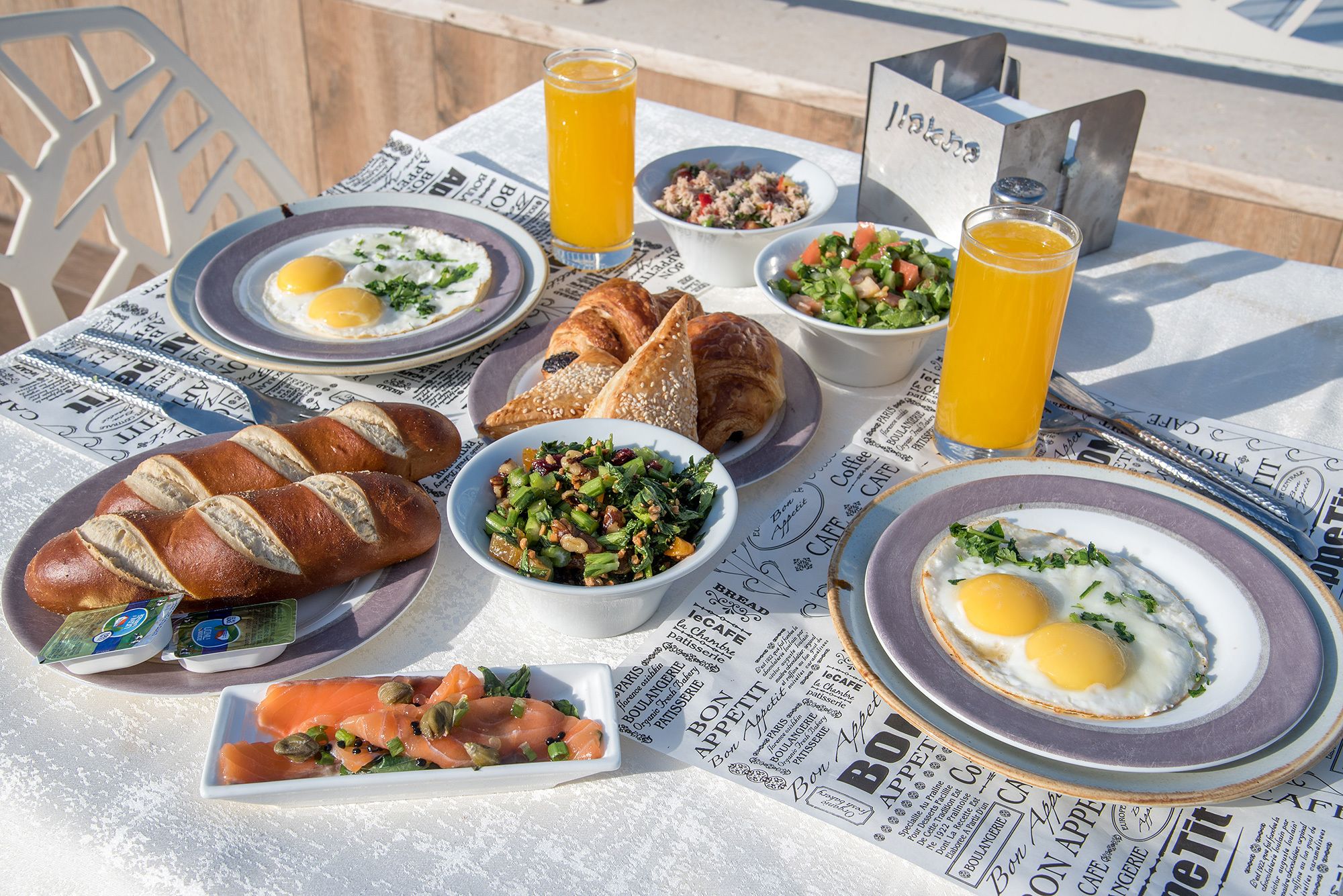 A breakfast setting with croissants, eggs, and various salads on a table with newspaper placemats.