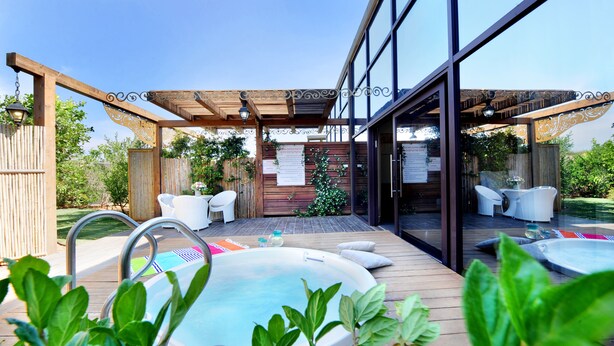 Ein Außenpoolbereich mit Whirlpools, Liegestühlen und einer Pergola mit hängenden Lichtern.