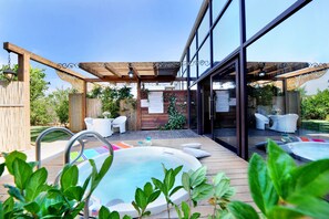 An outdoor pool area with hot tubs, lounge chairs, and a pergola with hanging lights.