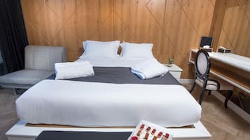 A hotel room with a large bed, a desk, a chair, and a small table with a tray of pastries.