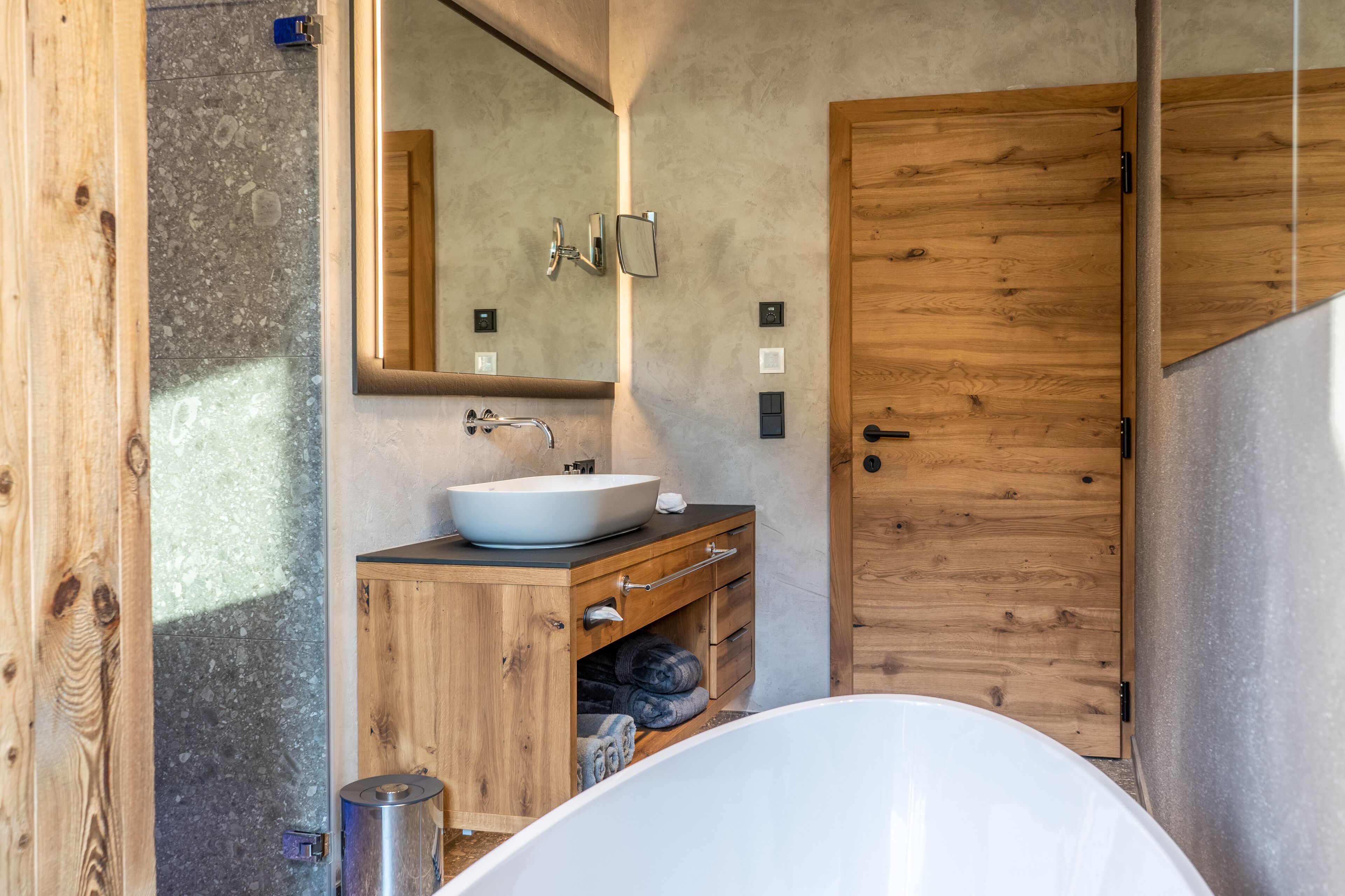 Un baño moderno con una bañera independiente, un tocador de madera con lavamanos y un espejo grande.