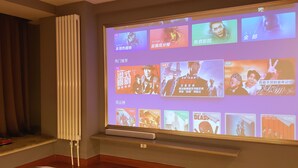 A projection screen displaying movie posters in a room with a radiator, a small table, and a shelf with books. - Xi'an Phoenix Holiday Hotel (Xi'an)