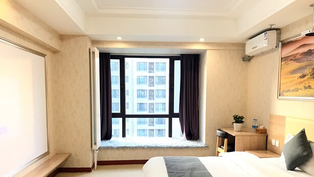 A hotel room with a large bed, a window with curtains, a small bedside table with a plant and water bottle, and an air conditioning unit on the wall. - Xi'an Phoenix Holiday Hotel (Xi'an)
