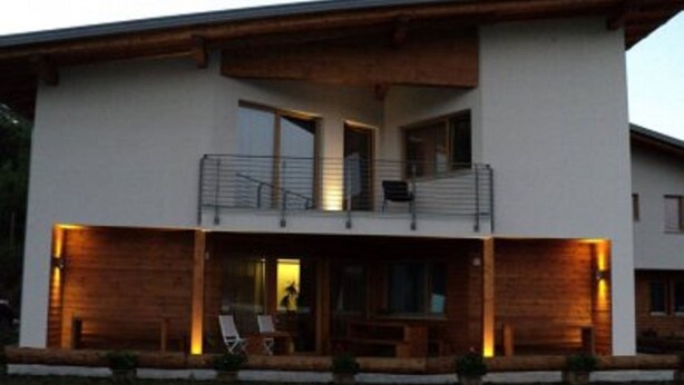 A two-story modern house with a balcony, large windows, and a well-lit porch area. - Agritur I Colori (Sanzeno)
