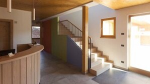 A reception area with a wooden counter, a staircase, and a door leading to another room. - Agritur I Colori (Sanzeno)