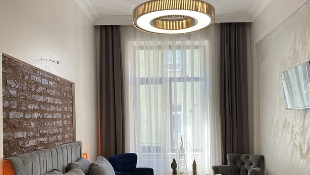 A modern bedroom with a large bed, a wooden nightstand, a blue armchair, a grey armchair, and a chandelier. - Galata Moon Hotel  (Istanbul)