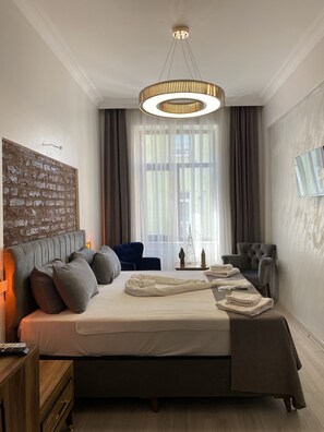 Ein modernes Schlafzimmer mit einem großen Bett, einem Holfnachtkästchen, einem blauen Sessel, einem grauen Sessel und einer Chandelüster.