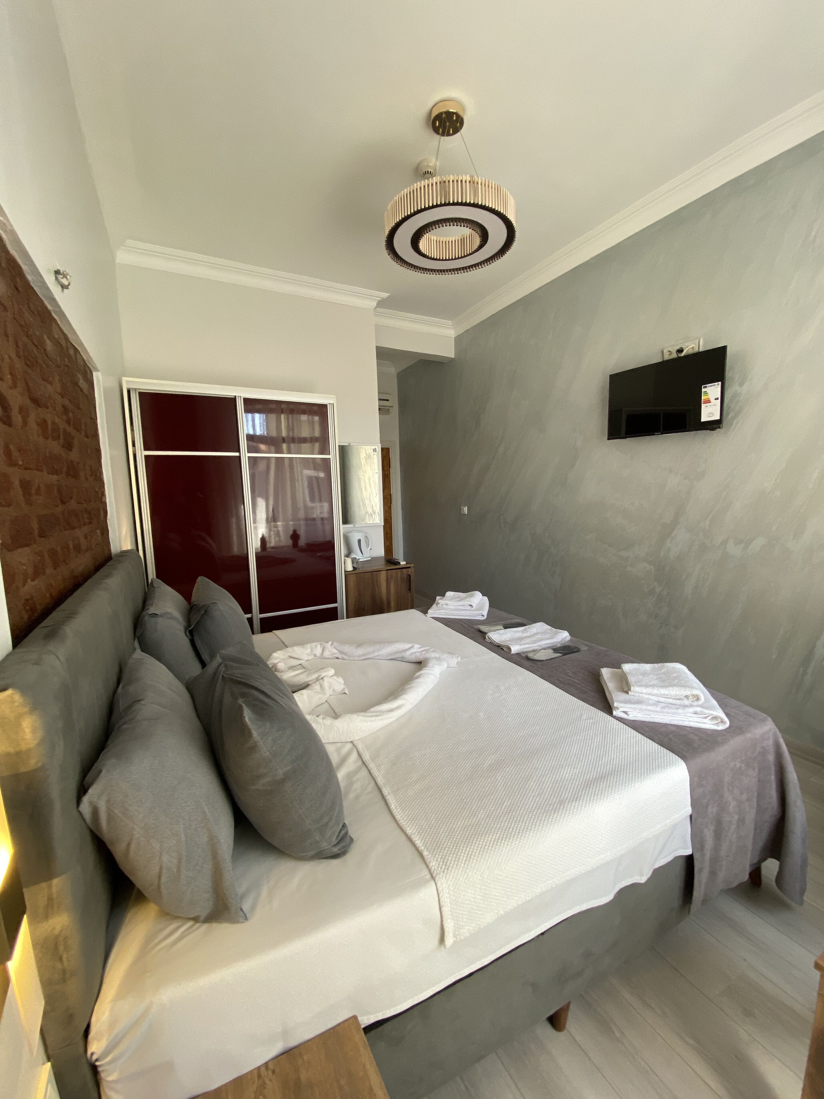 Une chambre d’hôtel avec un lit, un téléviseur fixé au mur, un mur en briques et une grande fenêtre.
