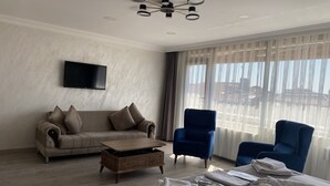 A modern hotel room with a sofa, two armchairs, a flat-screen TV, a wooden coffee table, and a bed with neatly folded towels. - Galata Moon Hotel  (Istanbul)