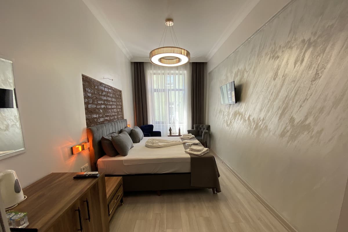 Quarto de hotel moderno com uma cama grande, uma escrivaninha de madeira, televisão e janela com cortinas.
