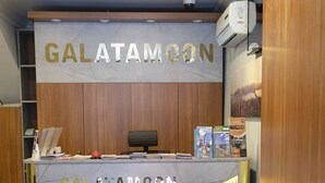 A reception desk with the name "GALATAMOON" in gold letters, a black office chair, a blue sofa, and a patterned carpet. - Galata Moon Hotel  (Istanbul)