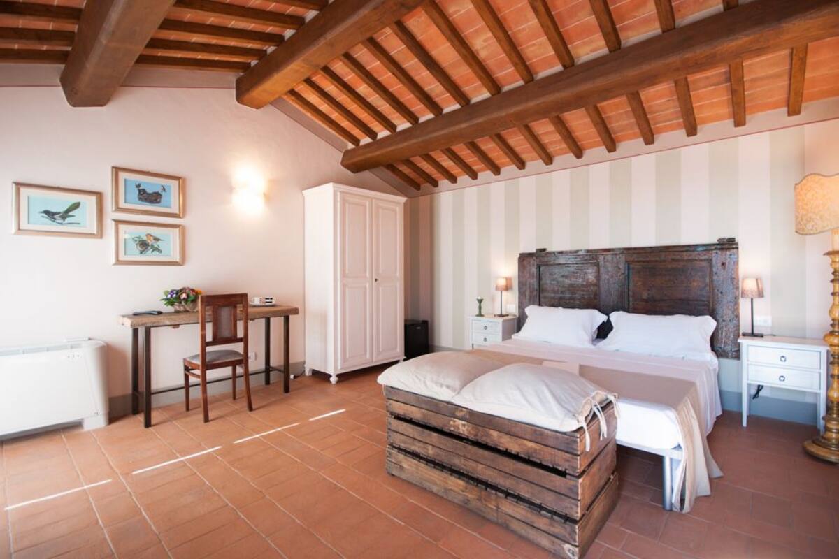 A bedroom with a rustic wooden headboard, a wooden bench, a white bed, a nightstand, a lamp, and a desk with a chair.