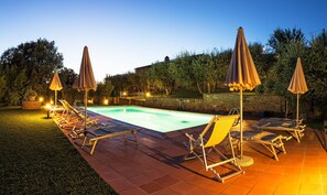 A swimming pool with lounge chairs and umbrellas, surrounded by a stone wall and trees. - Borgo tra gli Olivi (Castiglion Fiorentino)