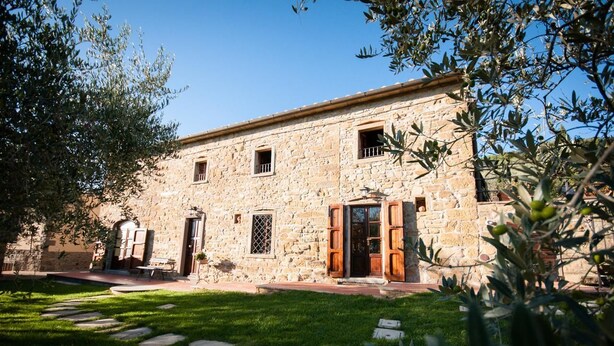 A stone building with a central door, windows, and a small table outside. - Borgo tra gli Olivi (Castiglion Fiorentino)