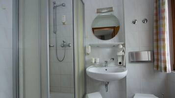 Ein modernes Badezimmer mit einer Glaskabine zur Dusche, einem weißen Waschbecken und einer Toilette.