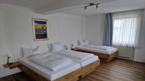 Een hotelkamer met twee houten bedden, een schilderij aan de muur en een raam met gordijnen.