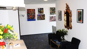 Een receptie met een wit bureau, zwarte stoelen, een bloemenvaas en verschillende abstracte schilderijen aan de muur.