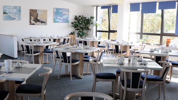 Een eetgedeelte met tafels en stoelen, kunst aan de muren en grote ramen.