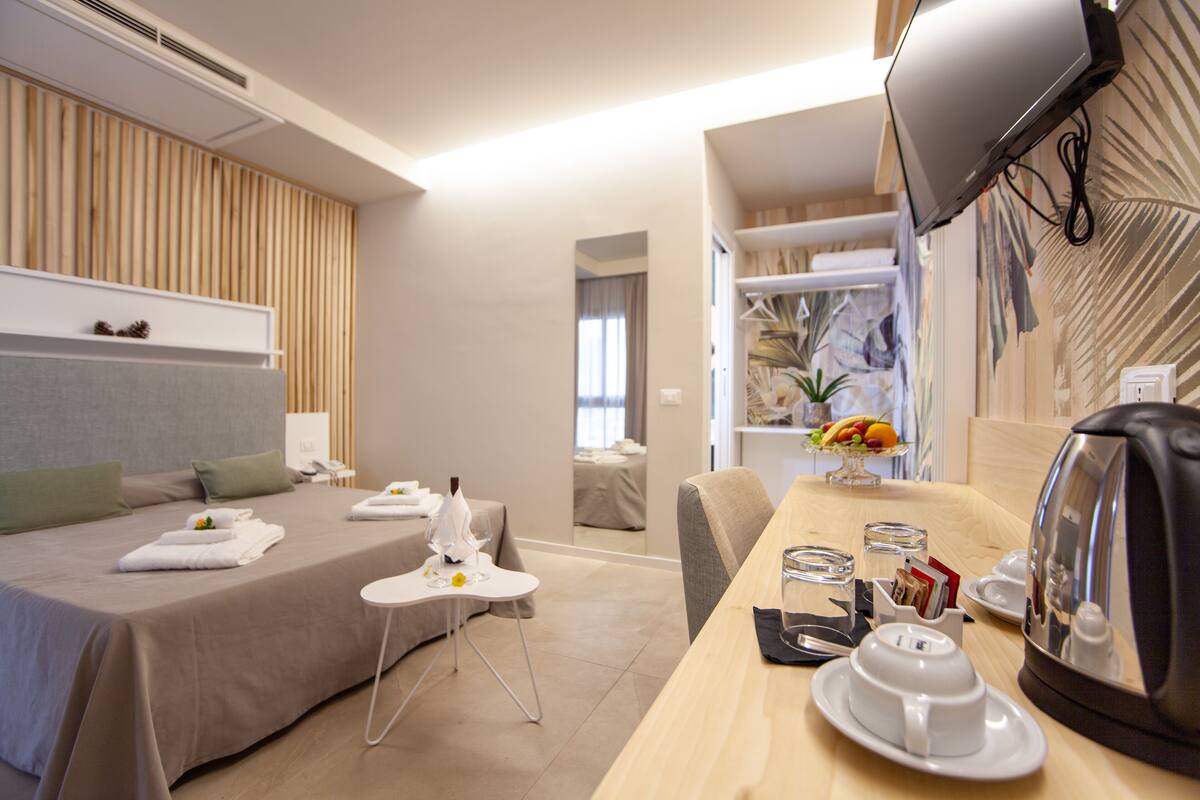 Une chambre d’hôtel comprenant un lit, une table de chevet et un coin repas avec une table, des chaises et une bouilloire.