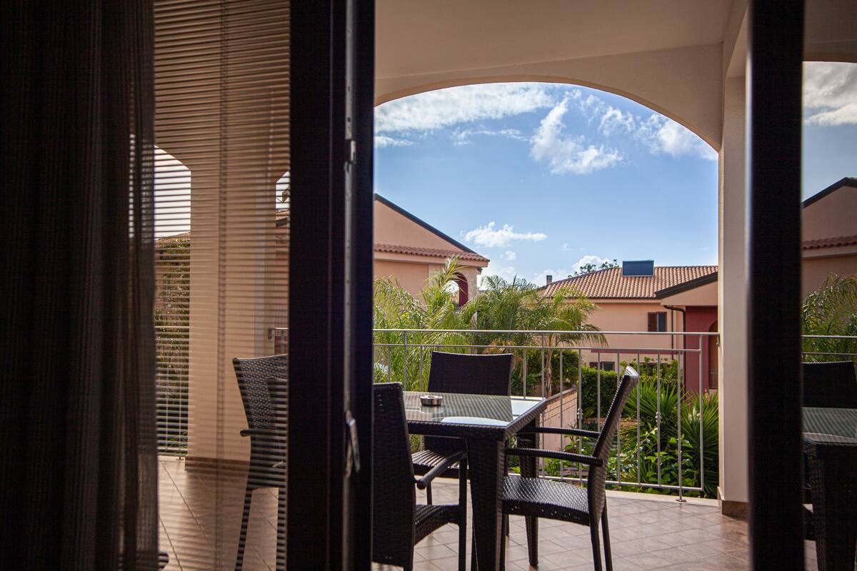 Un balcon avec une table et des chaises, une vue sur les bâtiments voisins et un ciel dégagé.