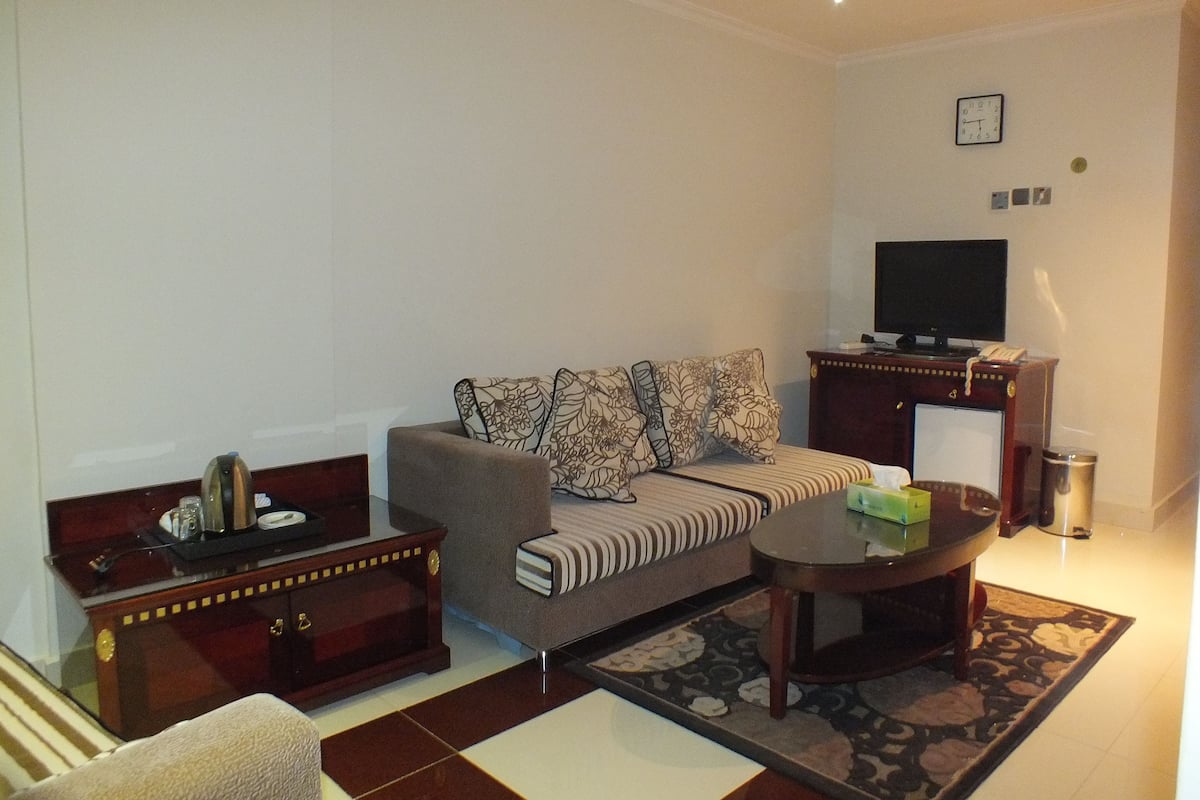 A living room with a sofa, a coffee table, a TV, a cabinet, and a trash can.