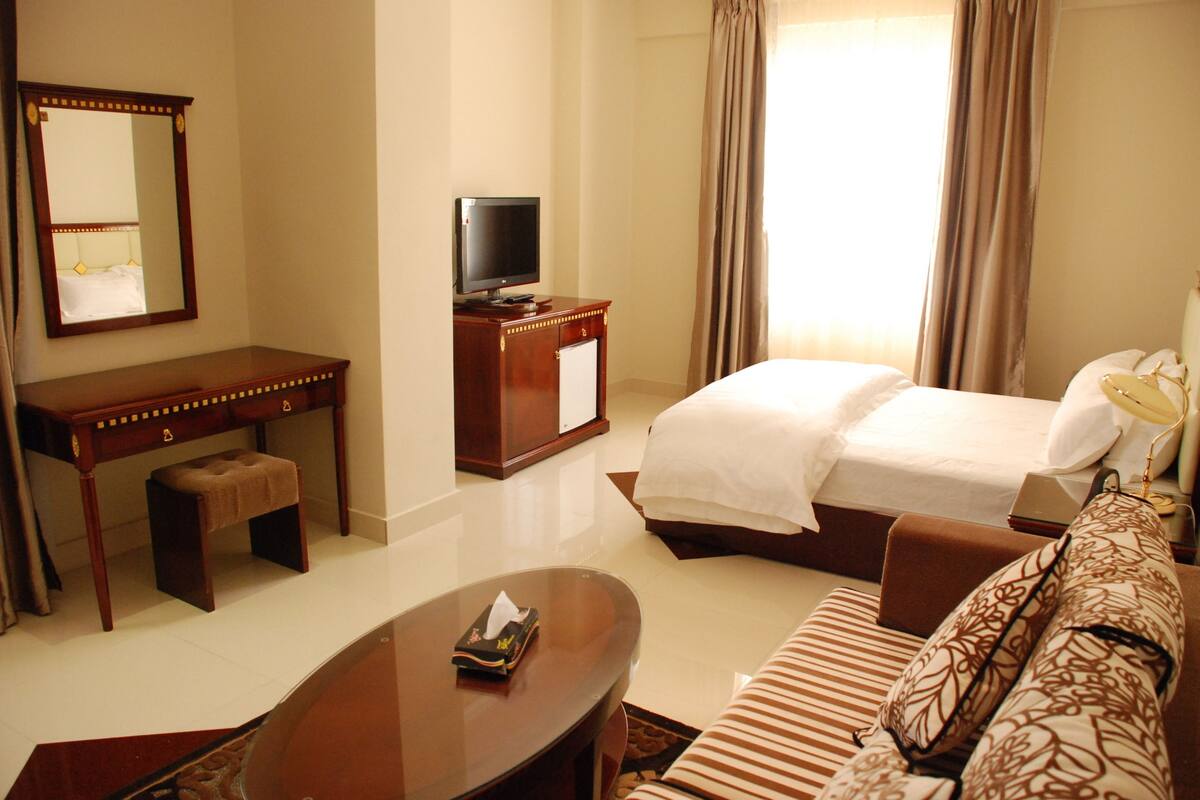 A hotel room with a bed, a sofa, a desk, a television, and a mirror.