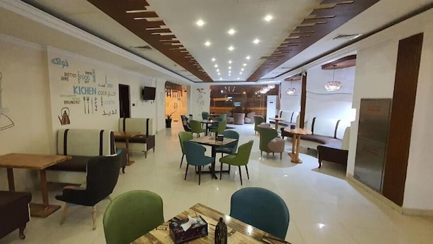 A modern dining area with multiple tables and chairs, a kitchen area, and a seating area with a counter. - City Hotel Salalah (Salalah)