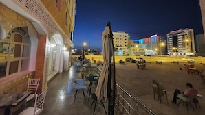 An outdoor seating area with tables and chairs, a covered section, and a view of the cityscape at night. - City Hotel Salalah (Salalah)