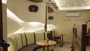 A modern interior with a curved sofa, round tables, and a wall with a 'Welcome to Roza Cafe' sign. - City Hotel Salalah (Salalah)