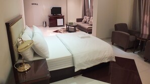 A hotel room with a bed, bedside table, lamp, TV, sofa, armchair, and curtains. - City Hotel Salalah (Salalah)
