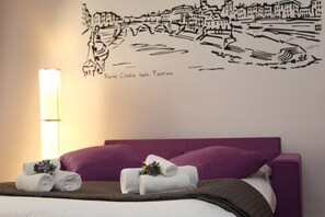 Una habitación de hotel con cama, ropa de cama morada, un mural en la pared y una lámpara.