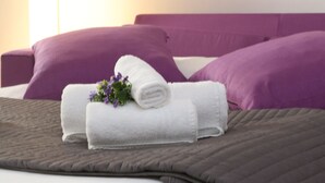 Une chambre d’hôtel avec un lit, une literie violette, une serviette blanche ornée de motifs floraux et une fresque murale représentant un pont et des bâtiments.