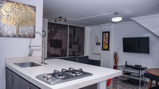 A modern kitchen with a central island, a dining area with a table and chairs, and a TV mounted on the wall. - Park Lleras 301 (Medellín)