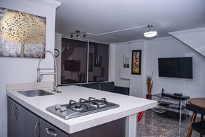 Een moderne keuken met een centraal eiland, een eethoek met tafel en stoelen, en een aan de muur bevestigde televisie.