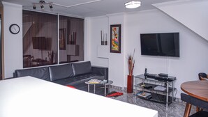 A modern living room with a grey sofa, a coffee table, a flat-screen TV mounted on the wall, and a dining area with a table and chairs. - Park Lleras 301 (Medellín)
