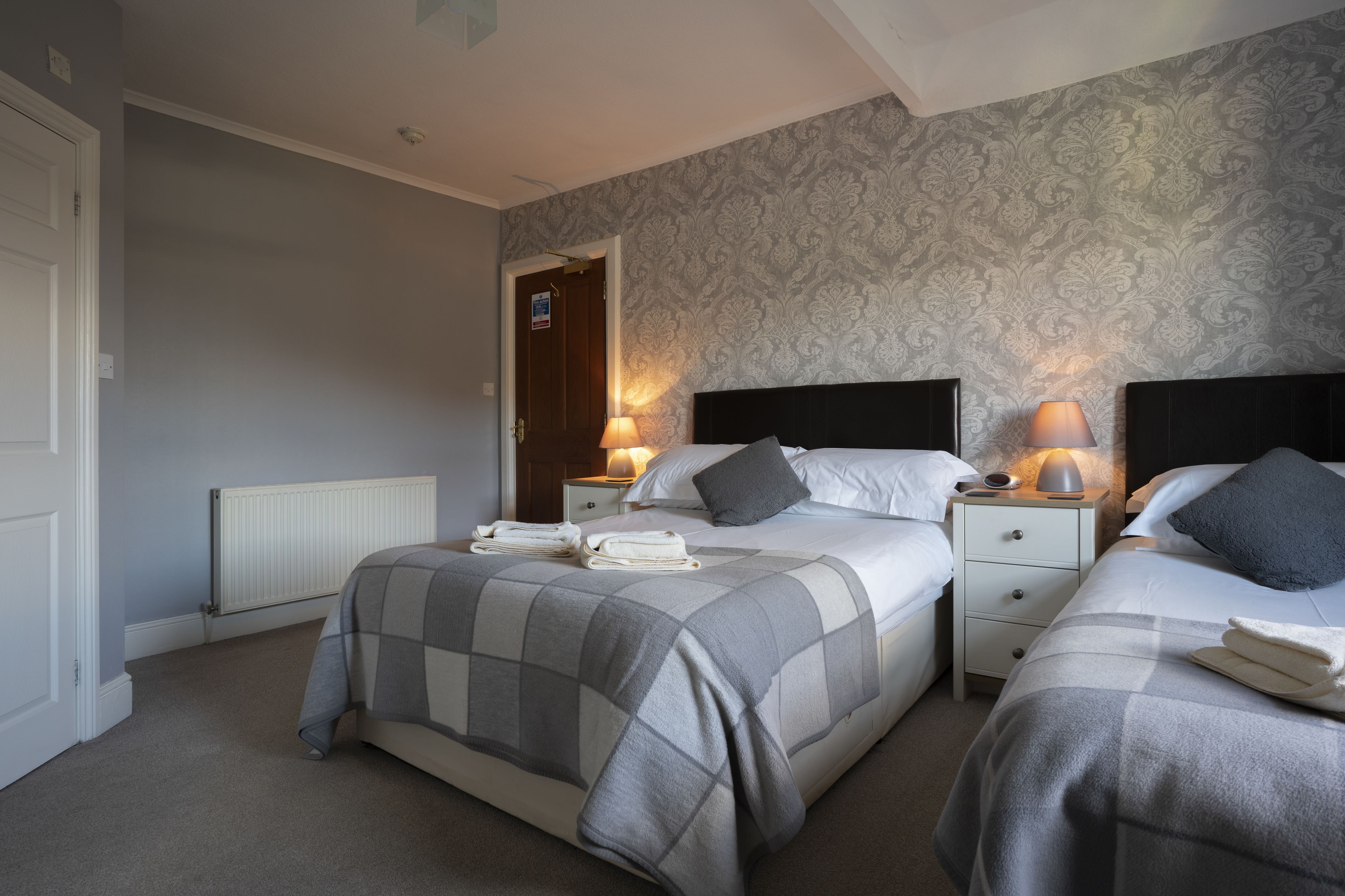 A double room with two beds, each with a headboard, bedside tables, lamps, and neatly folded towels.