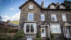 A stone building with multiple windows and a door, surrounded by a wooden fence and greenery. - Lyndale Guest House (Ambleside)