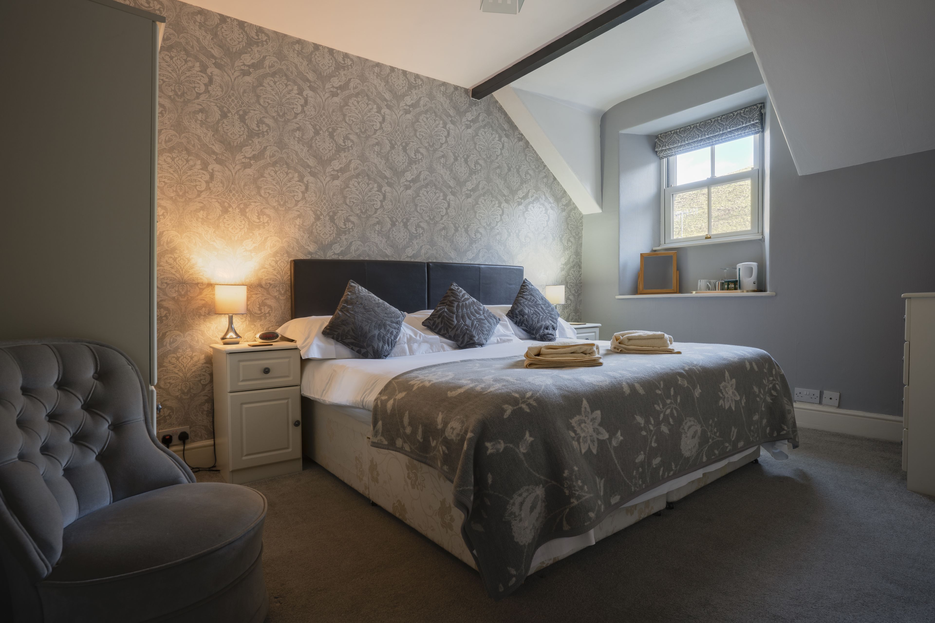A bedroom with a large bed, a nightstand, a chair, and a window with a view.