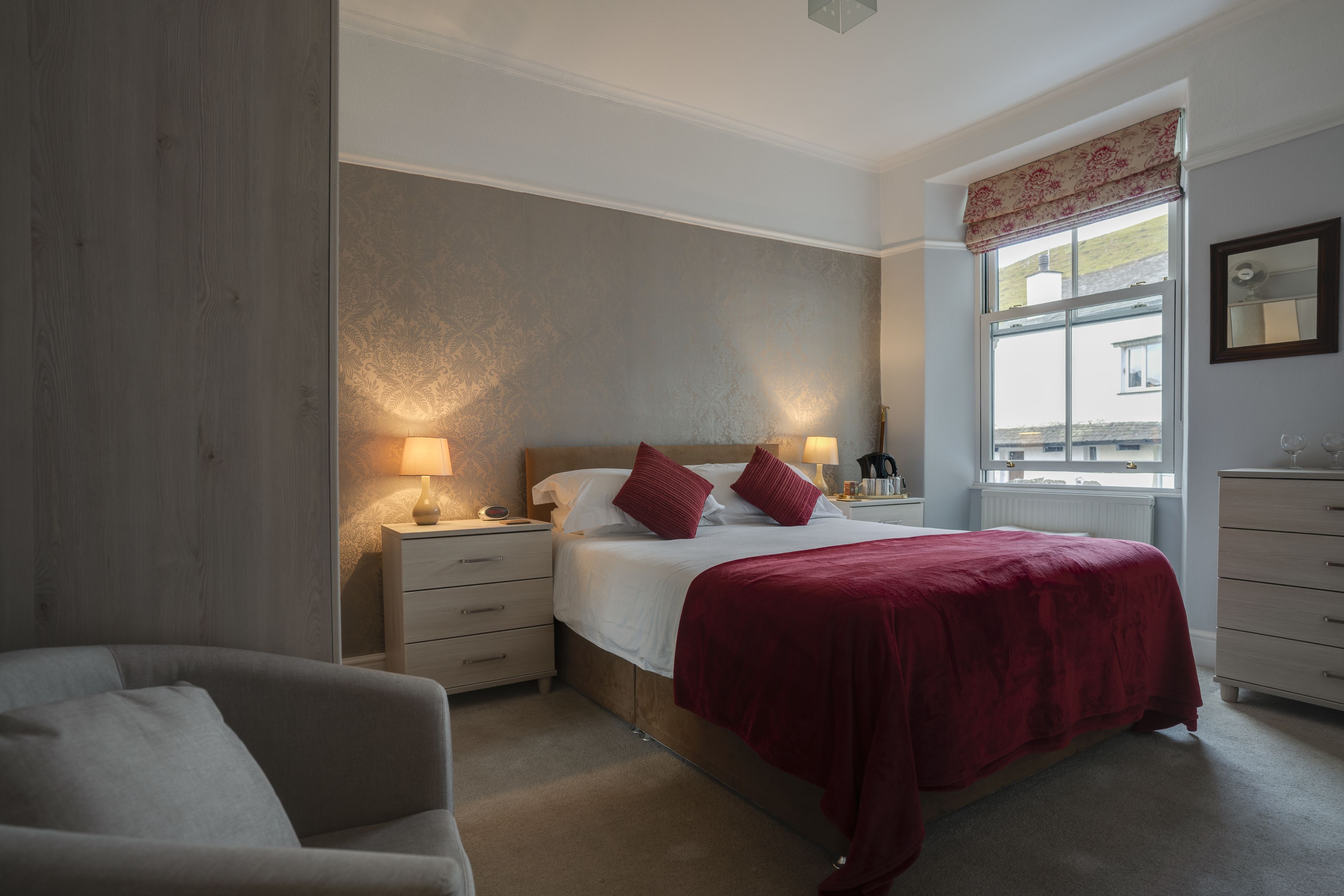 A bedroom with a large bed, two bedside tables with lamps, a dresser, and a window with a view of the outside.