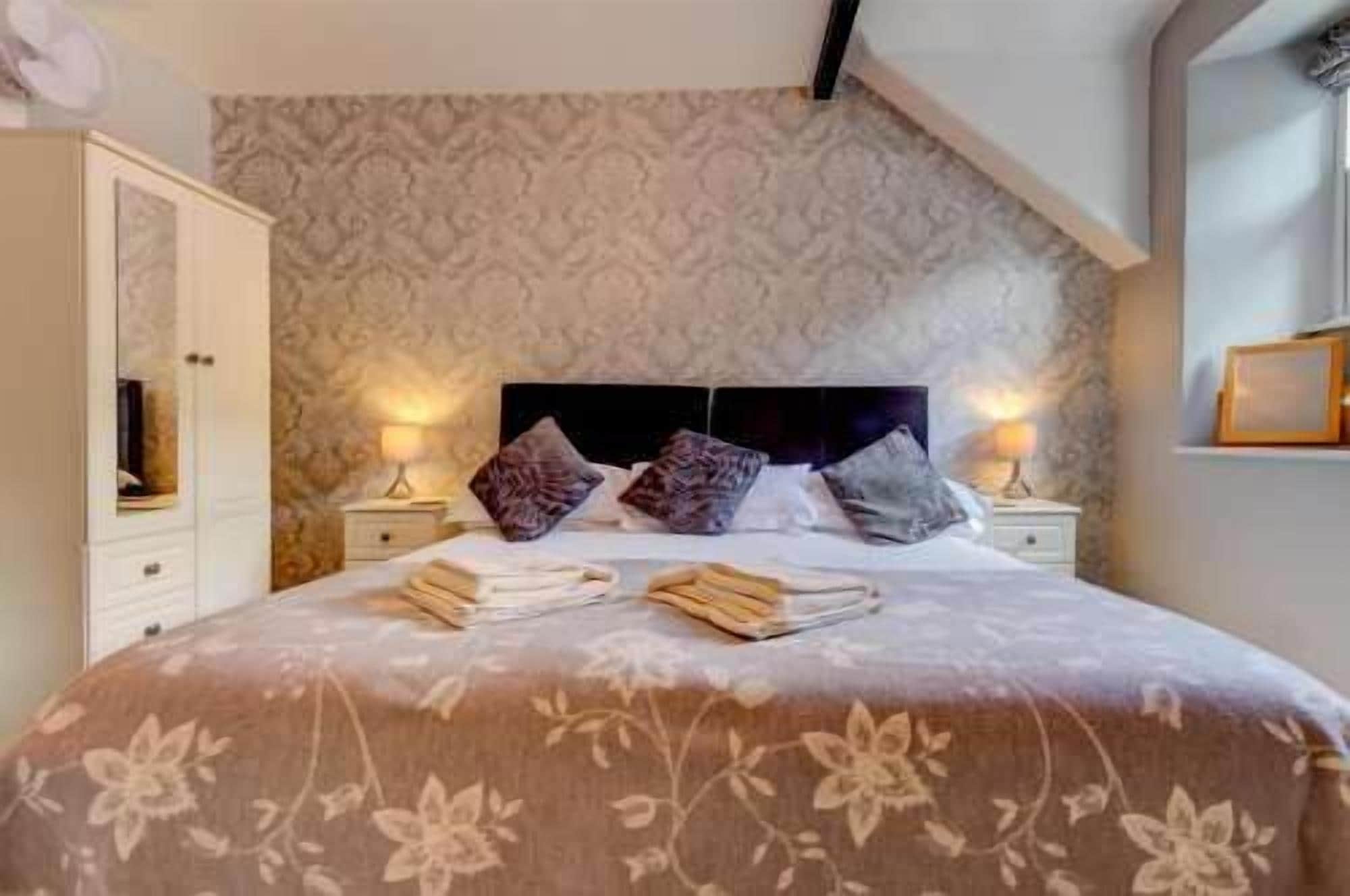 Une chambre avec un grand lit, deux tables de chevet, une armoire et un papier peint à motifs.
