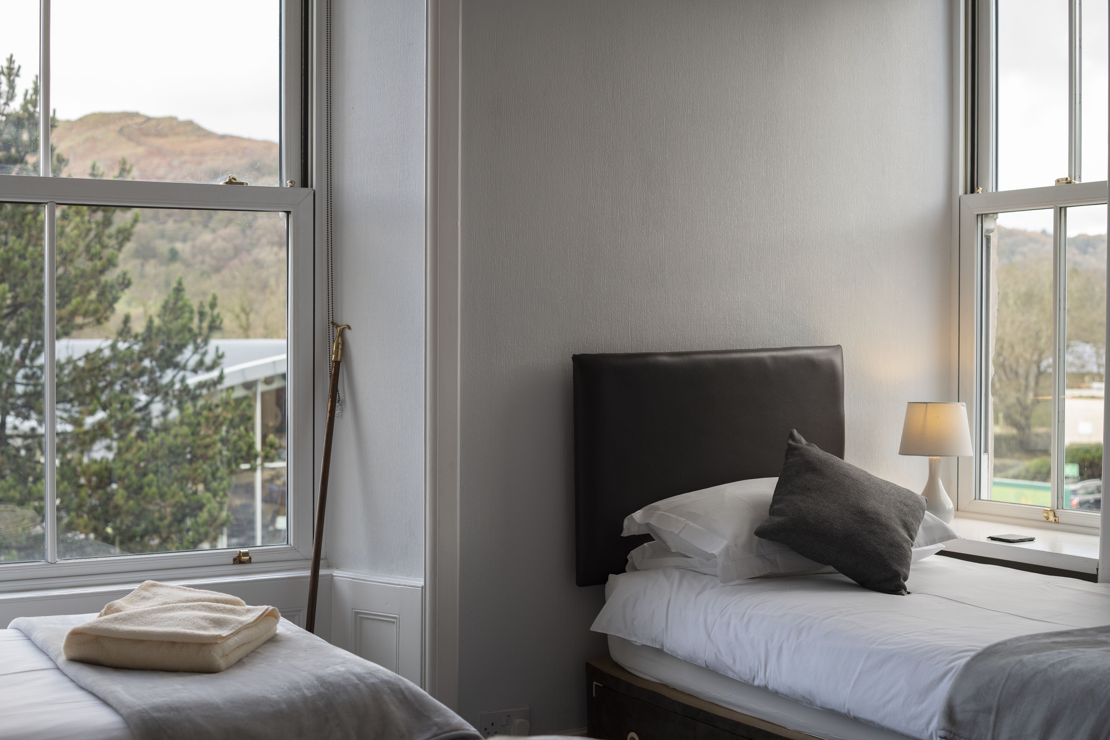 A hotel room with a bed, bedside table, lamp, and a view of a mountain through a window.