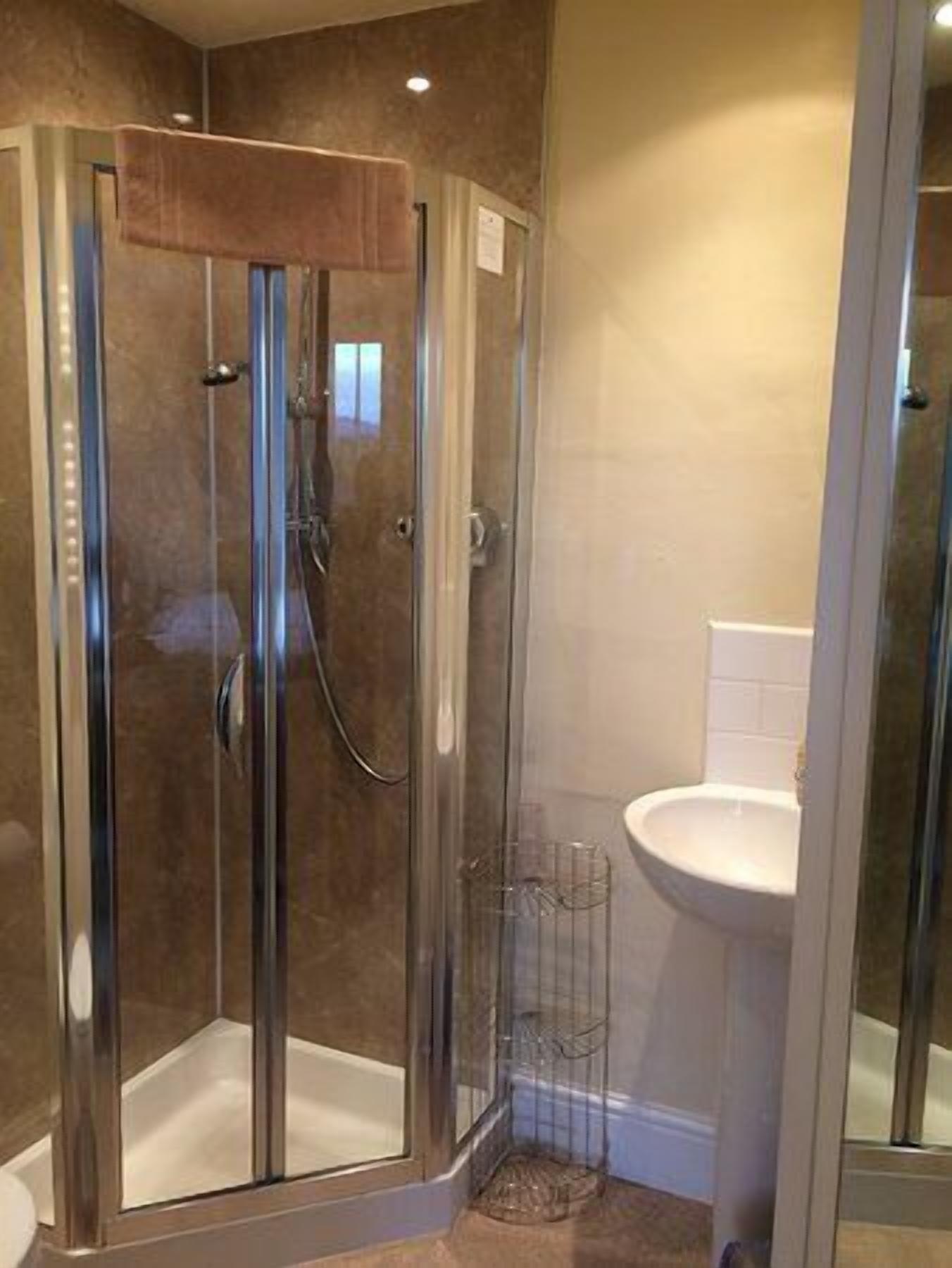 A glass-enclosed shower with a handheld showerhead and a handheld faucet.