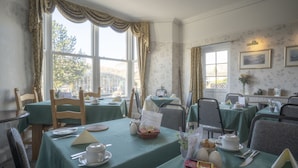A dining area with tables set for breakfast, featuring green tablecloths, white plates, and various breakfast items. - Lyndale Guest House (Ambleside)