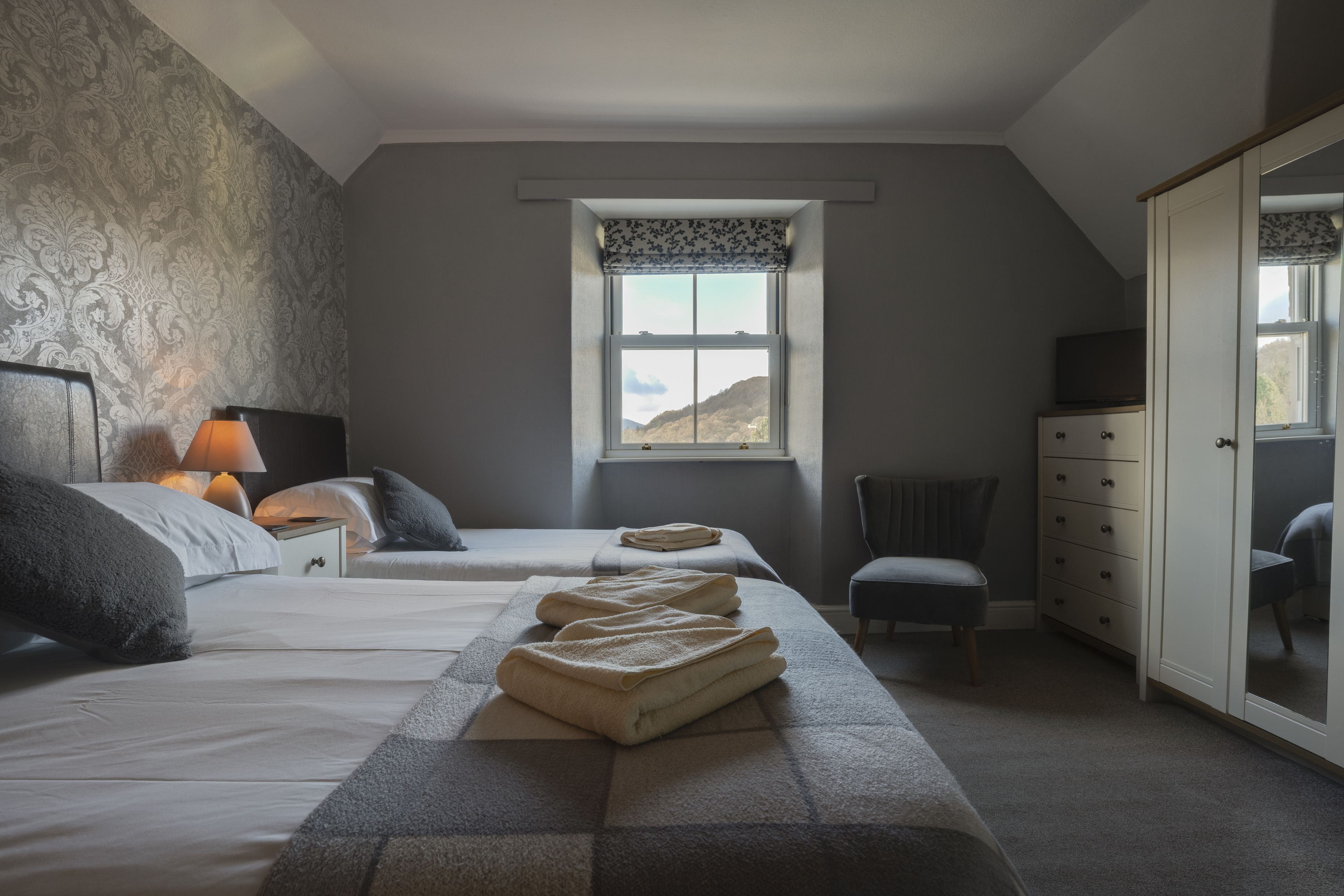 A bedroom with two beds, a window with a view, a dresser, and a chair.