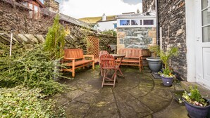 A stone building with a patio area featuring wooden furniture and potted plants. - Lyndale Guest House (Ambleside)