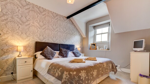 A bedroom with a large bed, a nightstand, a TV, and a window with a view. - Lyndale Guest House (Ambleside)