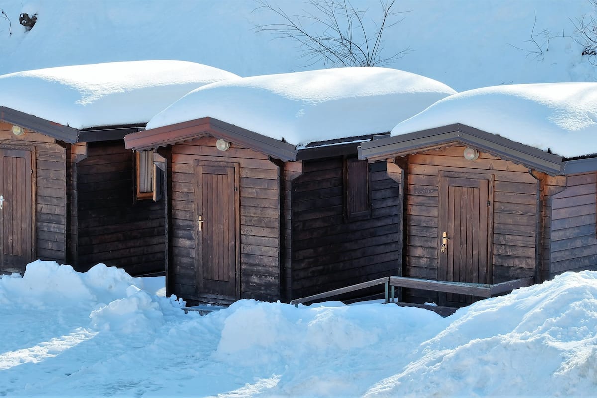 Una hilera de cabañas de madera cubiertas de nieve, con un cielo despejado al fondo.