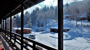 Eine Holzhütte mit Veranda mit Blick auf eine verschneite Landschaft, Bäume und einen Reisemobilwagen.